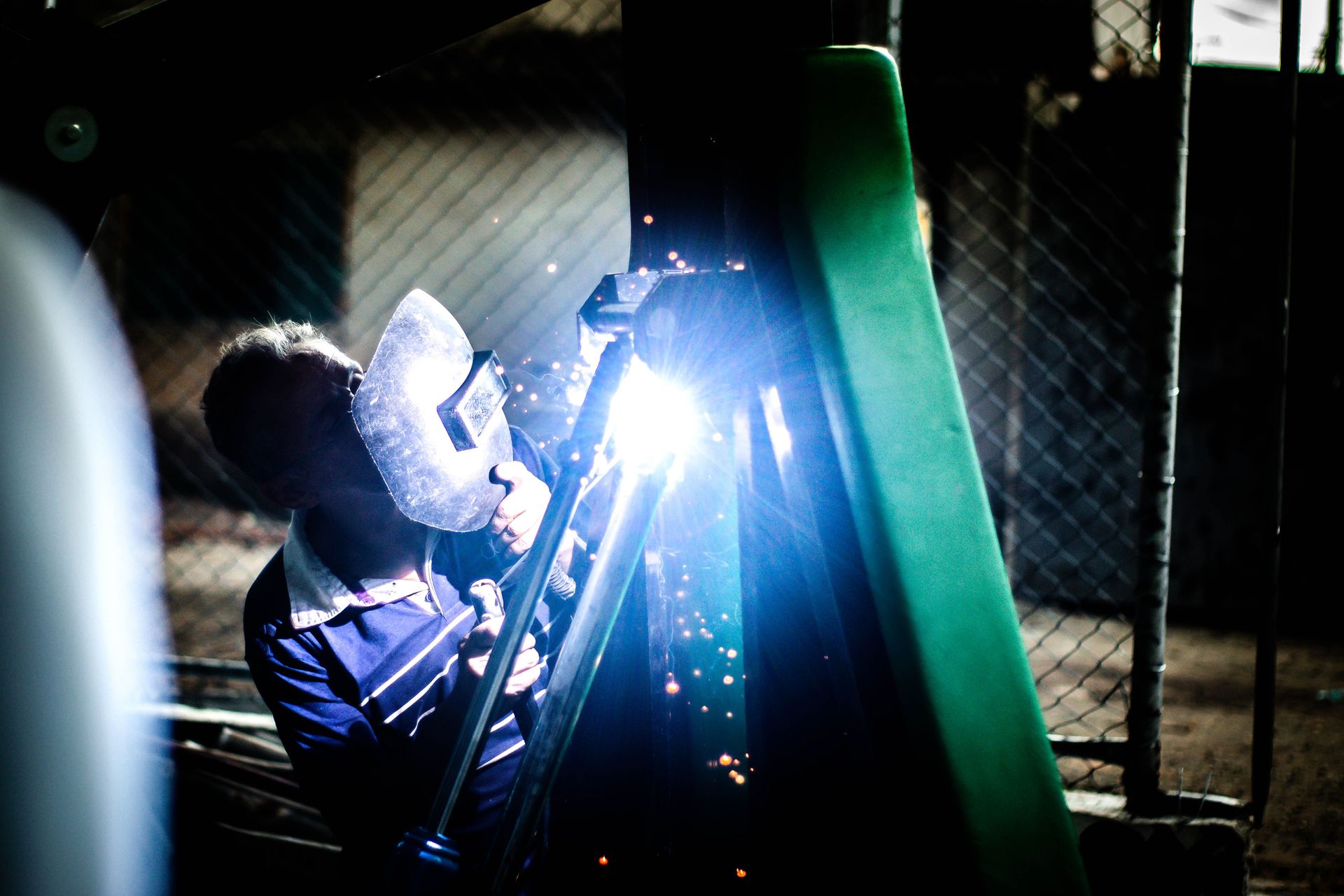 Anonymous male welder holding mask in front of face while working with equipment near fence poles at night