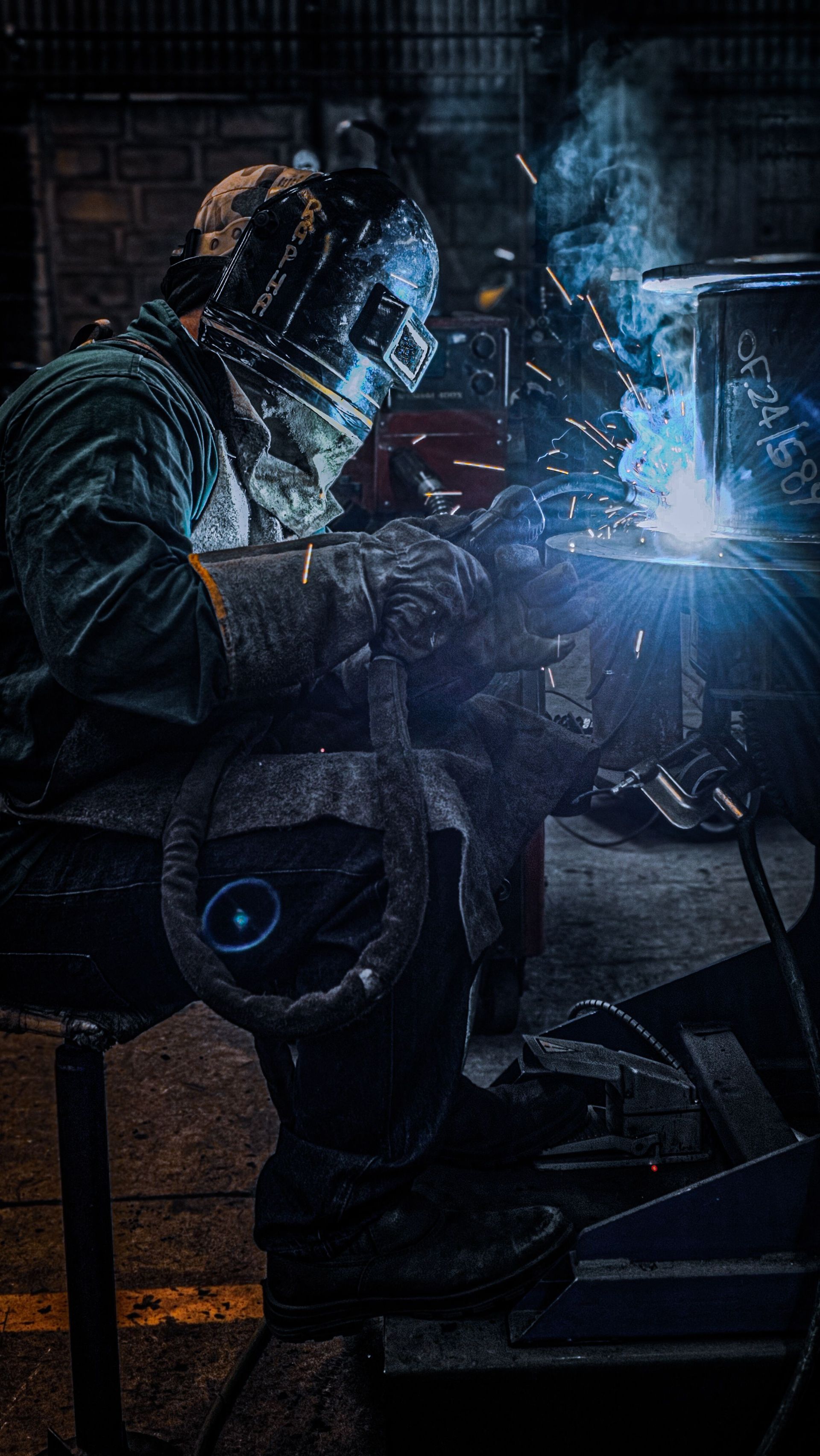 Welder working with bright sparks and smoke in a dimly lit workshop. Industrial scene.