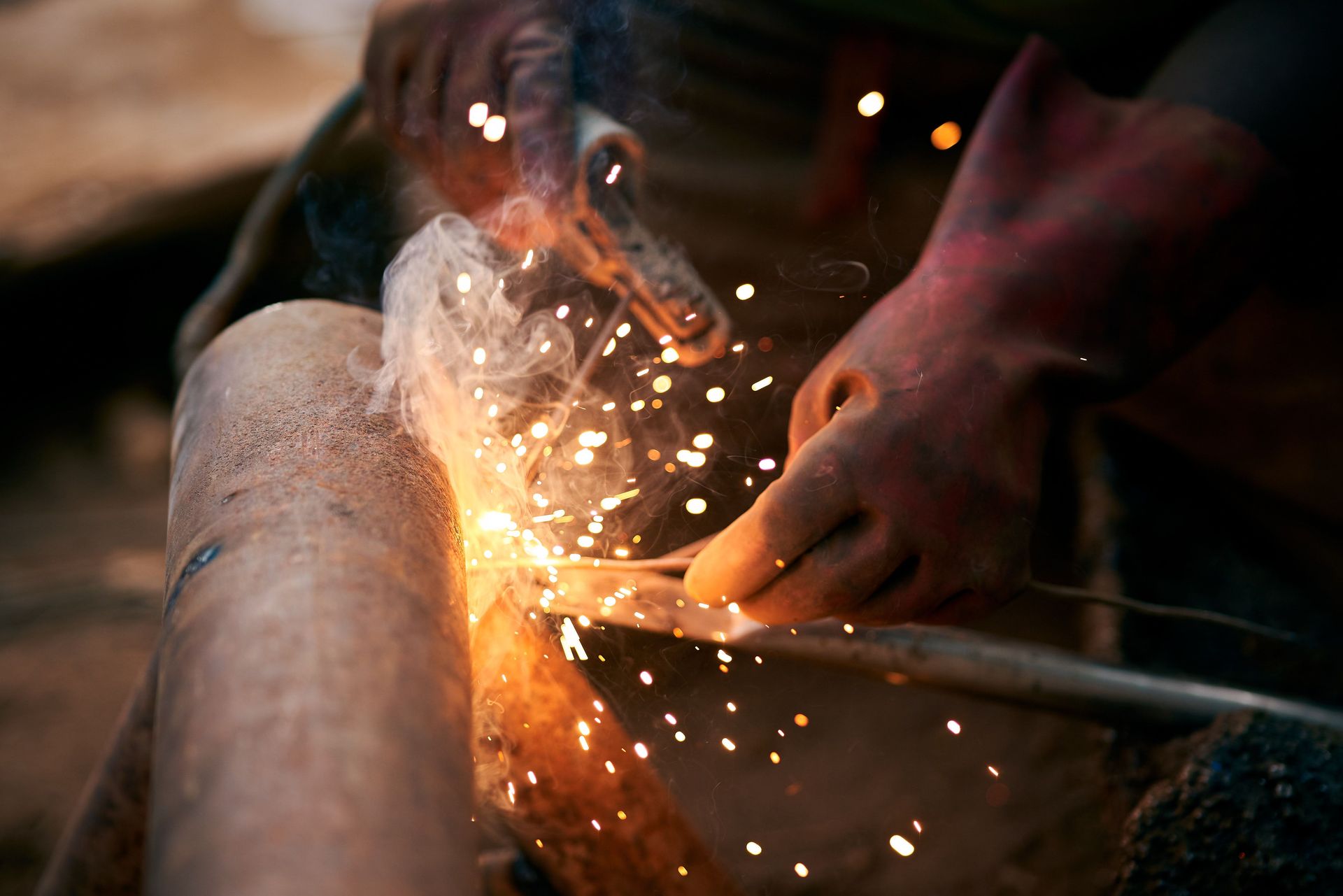 Detailed view of a welder's hands with gloves as sparks fly during welding.