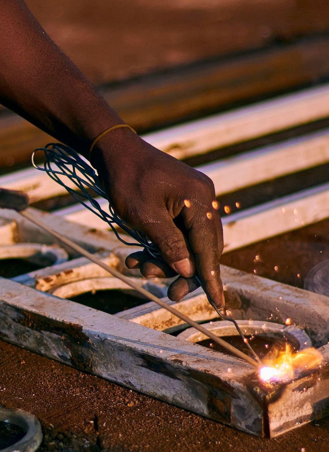 A welder performing metalwork on a gate with sparks flying, captured during dusk.