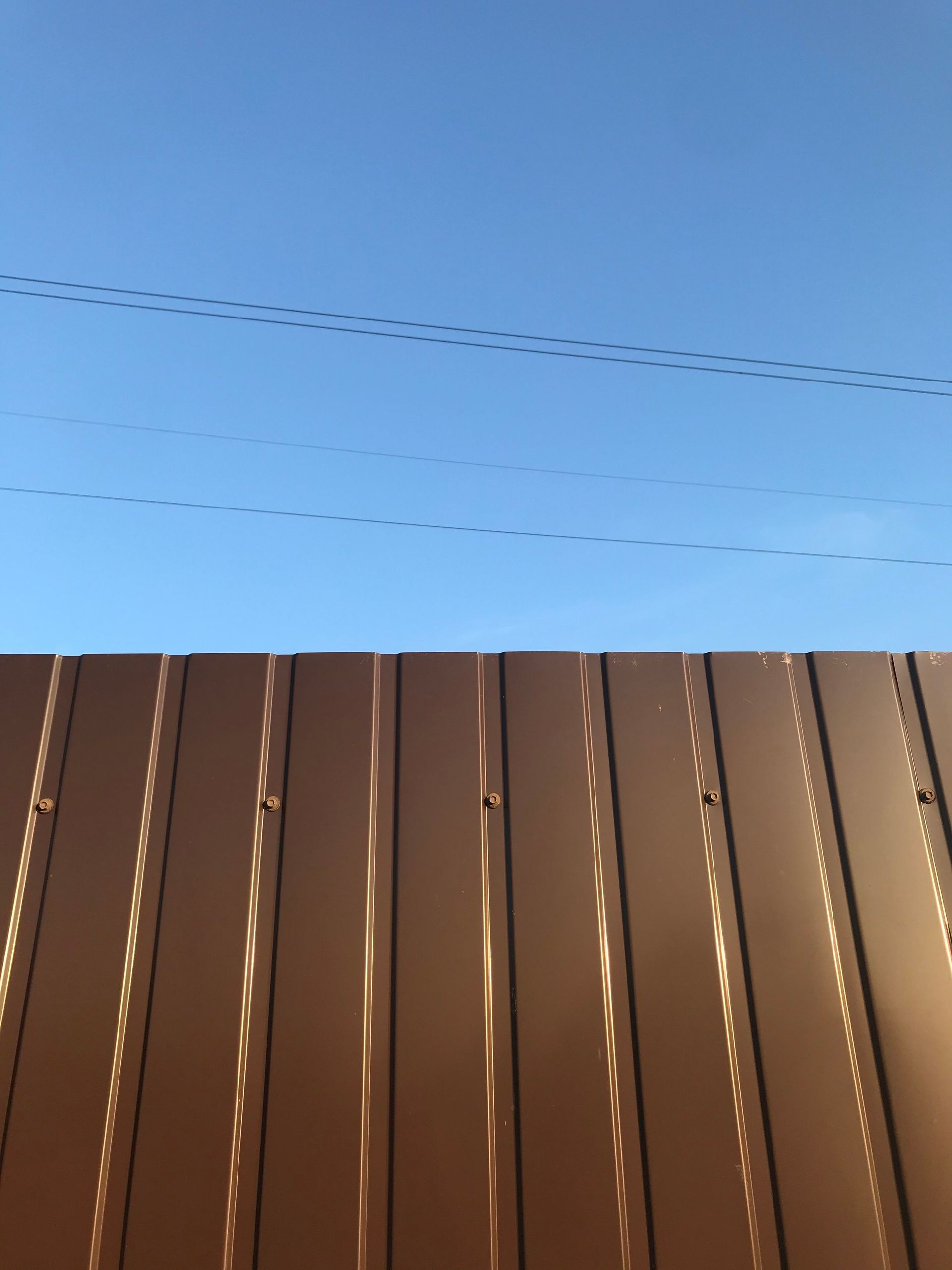 Photograph of a brown metal fence under a clear blue sky, offering a minimalist and modern look.