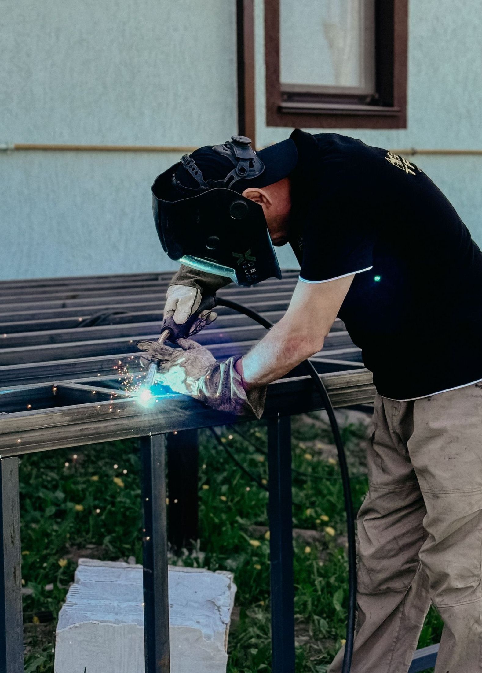A worker wearing protective gear skillfully welds metal outdoors, showcasing industrial craftsmanship.