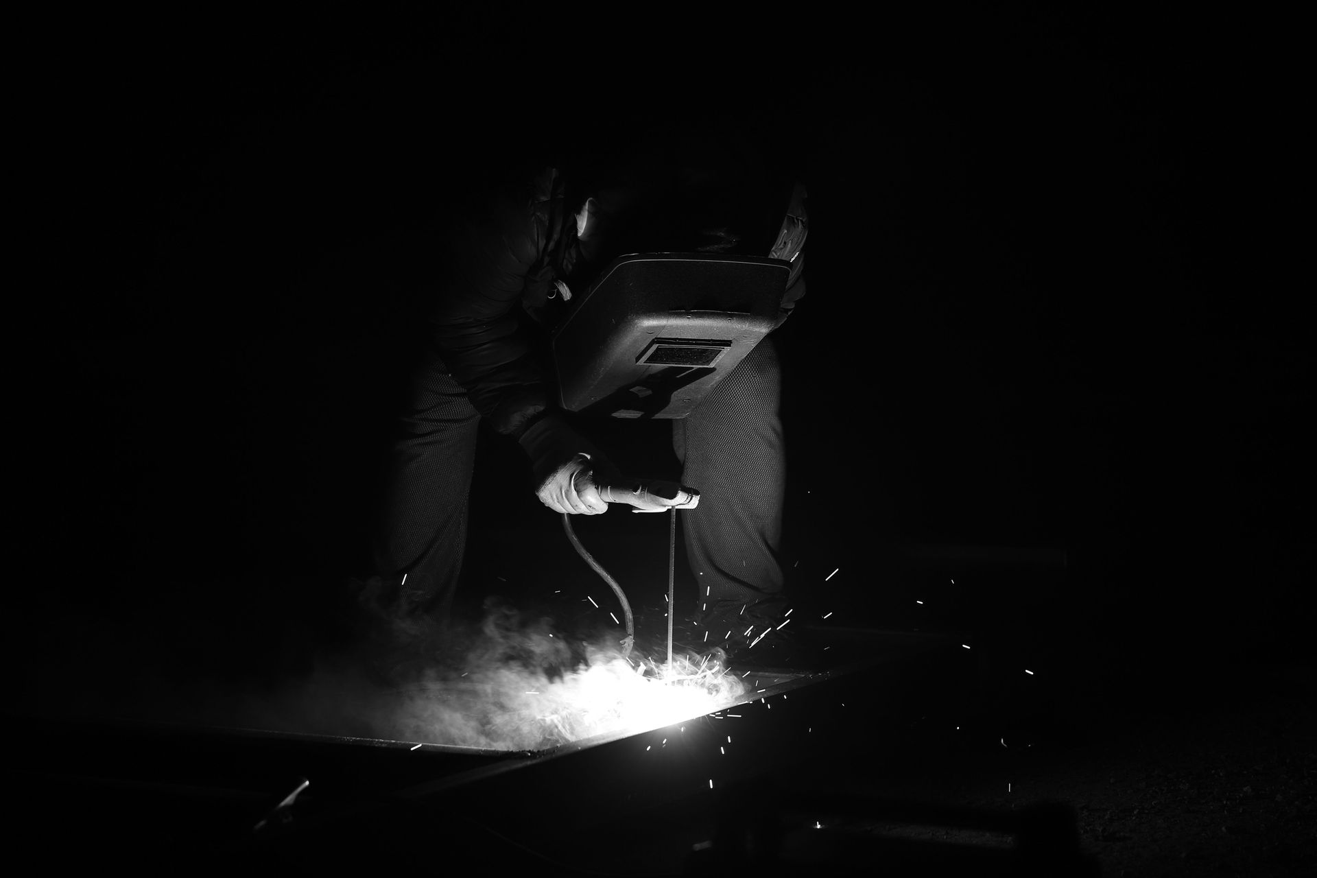 Black and white photo of a welder working with sparks flying in a dark setting.
