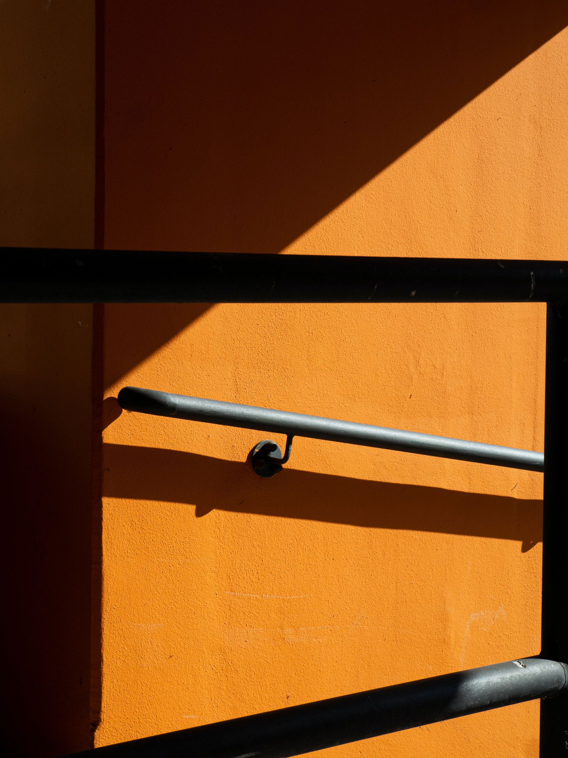 Close-up of a handrail casting shadows on an orange wall, evoking a modern minimalist feel.
