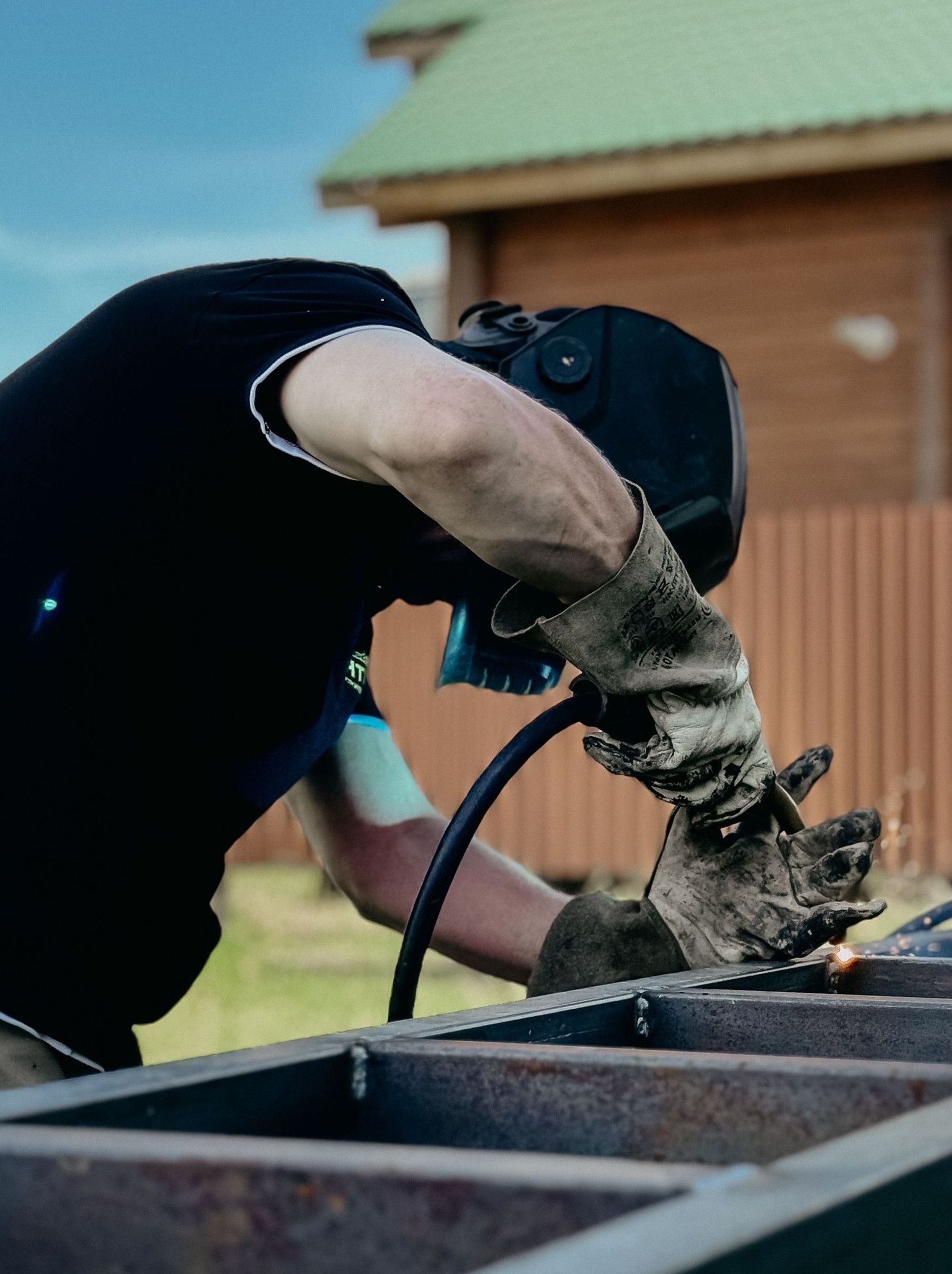 A welder working on a metal structure outdoors in a workshop setting.