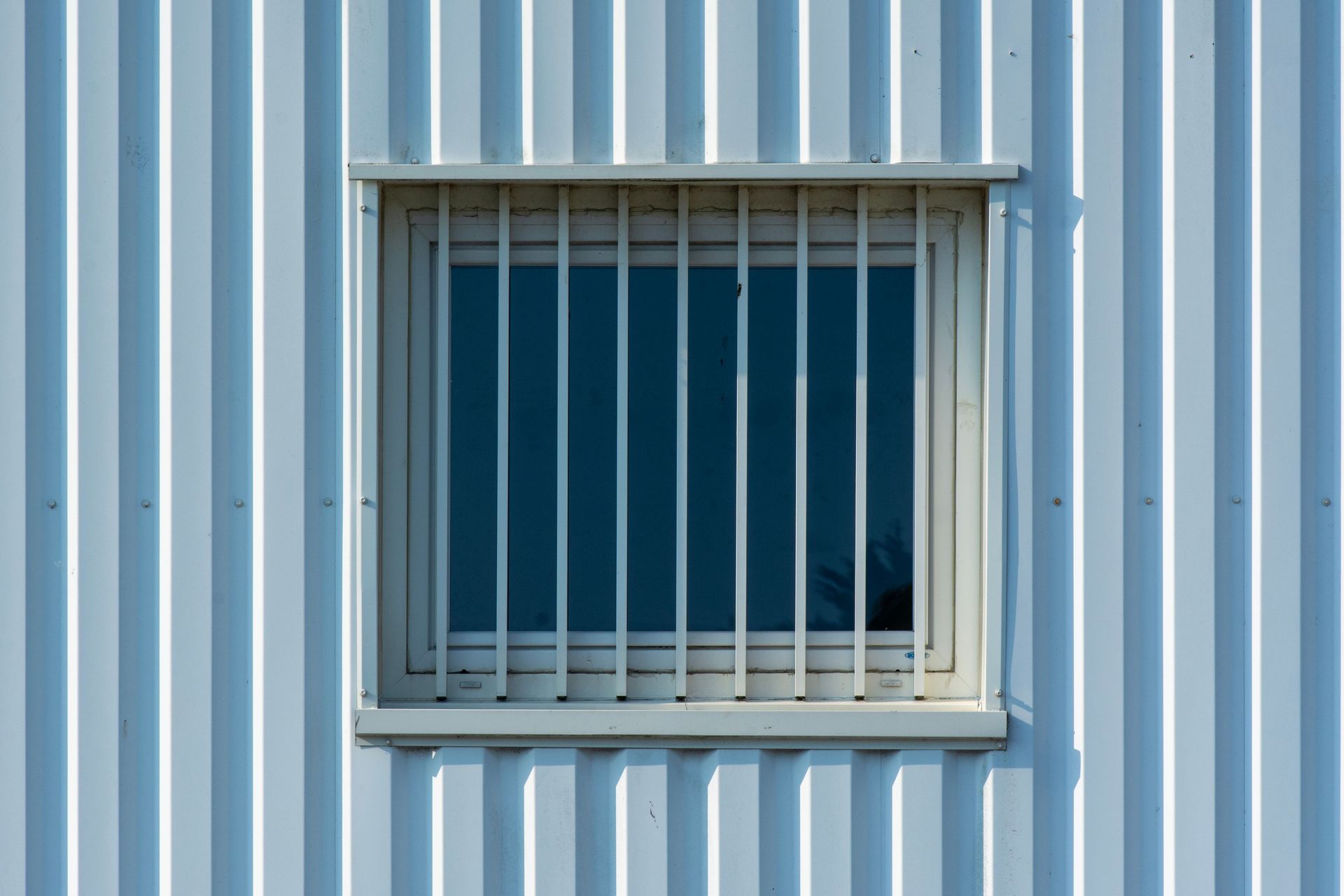 Close-up of a barred window on a corrugated metal building facade, emphasizing urban architecture.