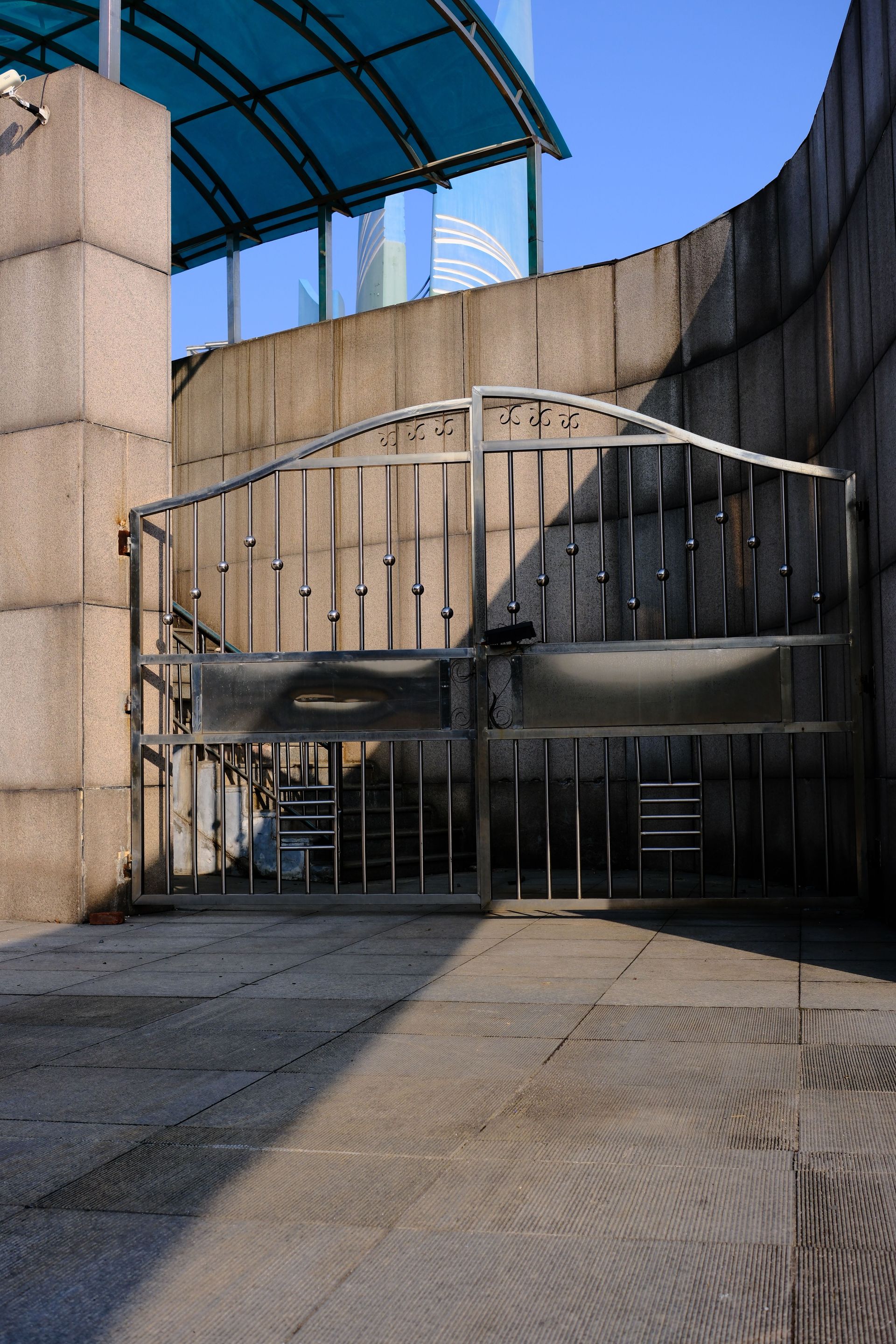 An urban industrial metal gate with concrete walls under clear blue skies.
