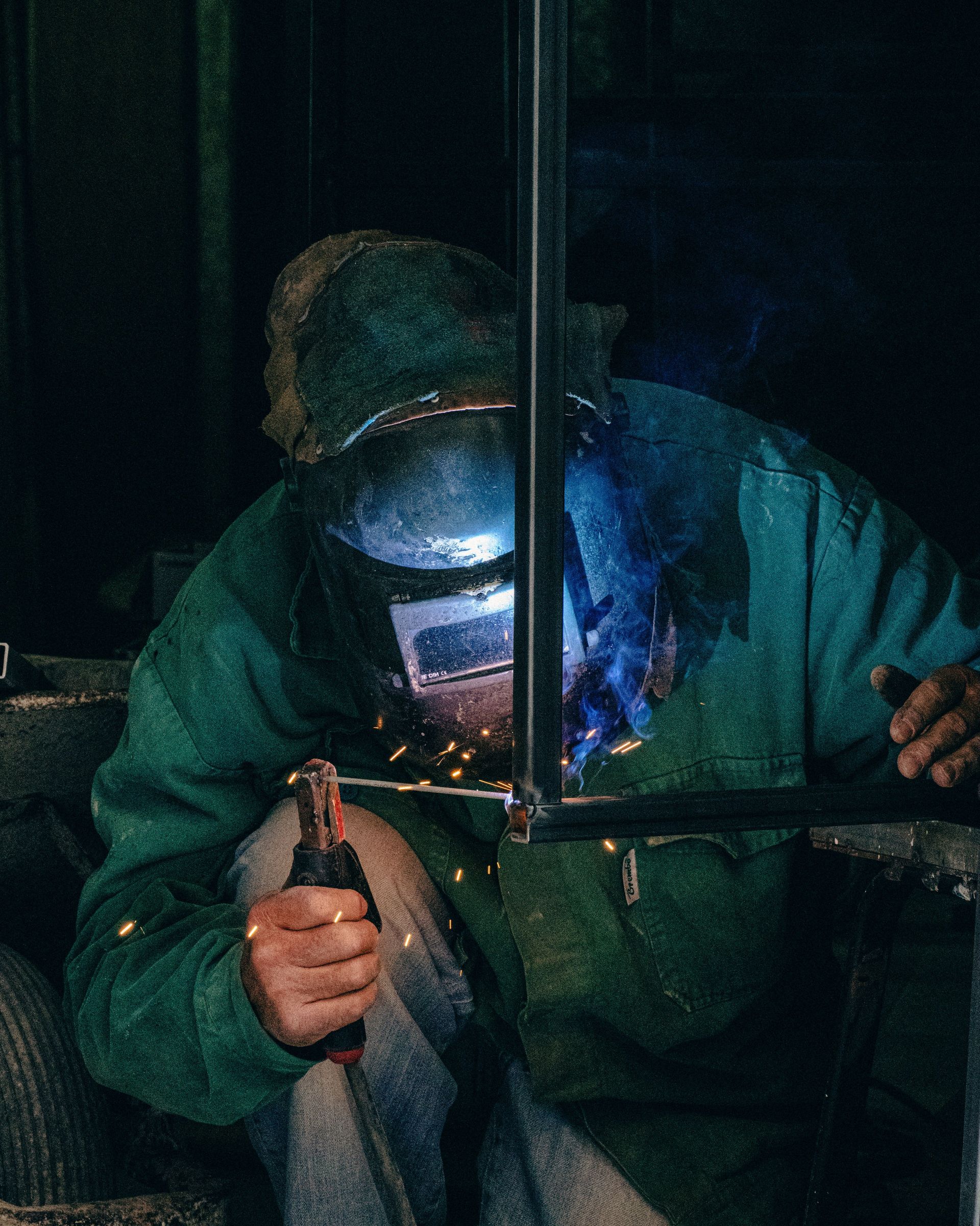 Welder using equipment in a Mellieħa workshop, garbed in safety gear with welding sparks.