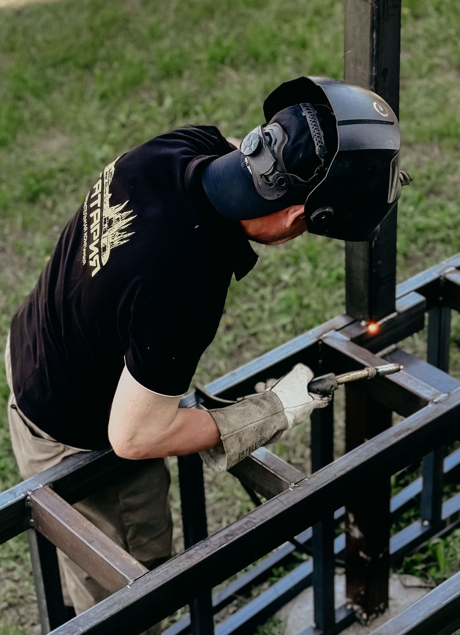 A welder in protective gear working on a metal frame in an outdoor setting.