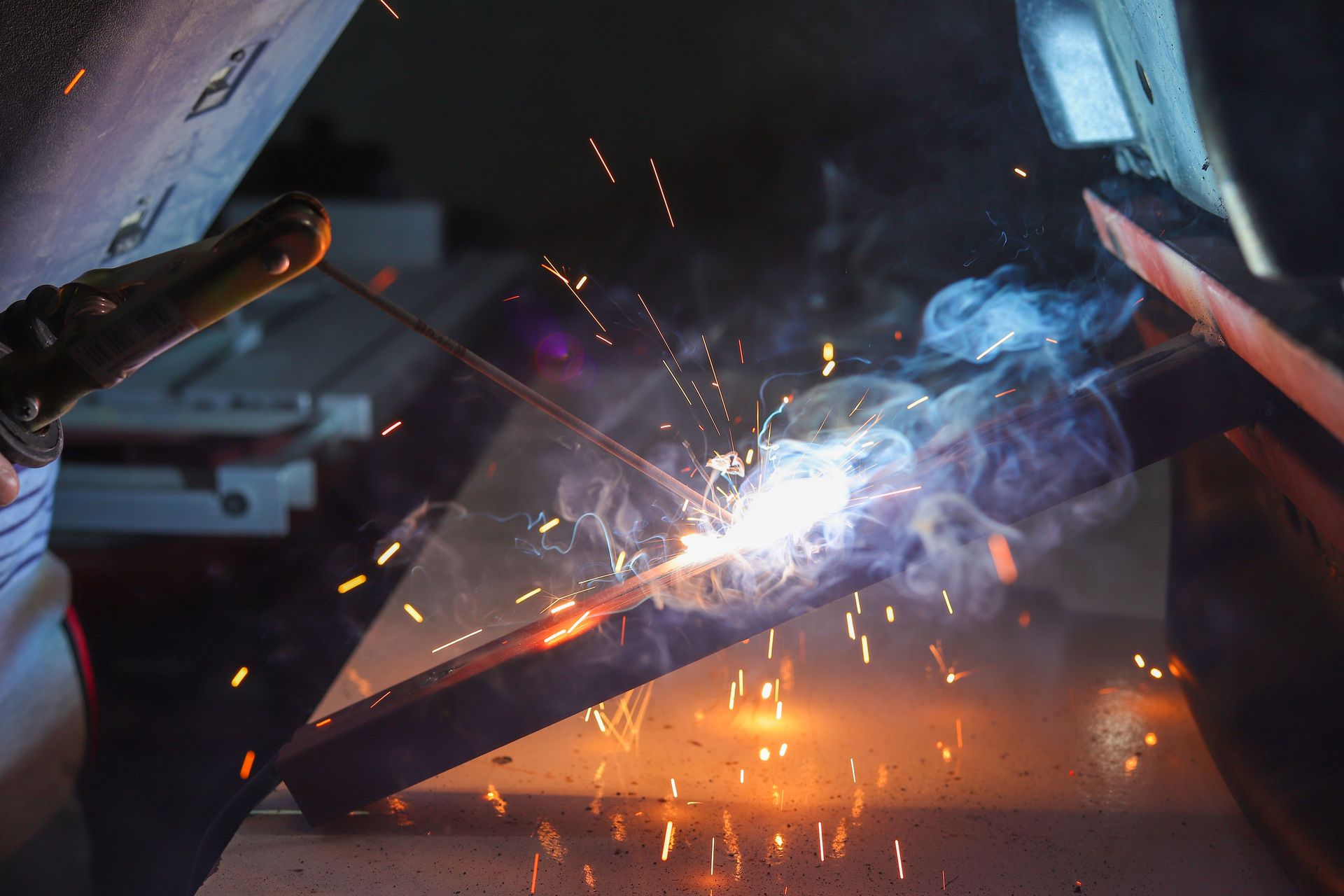 Close-up of a welder at work with sparks and smoke in an industrial setting.
