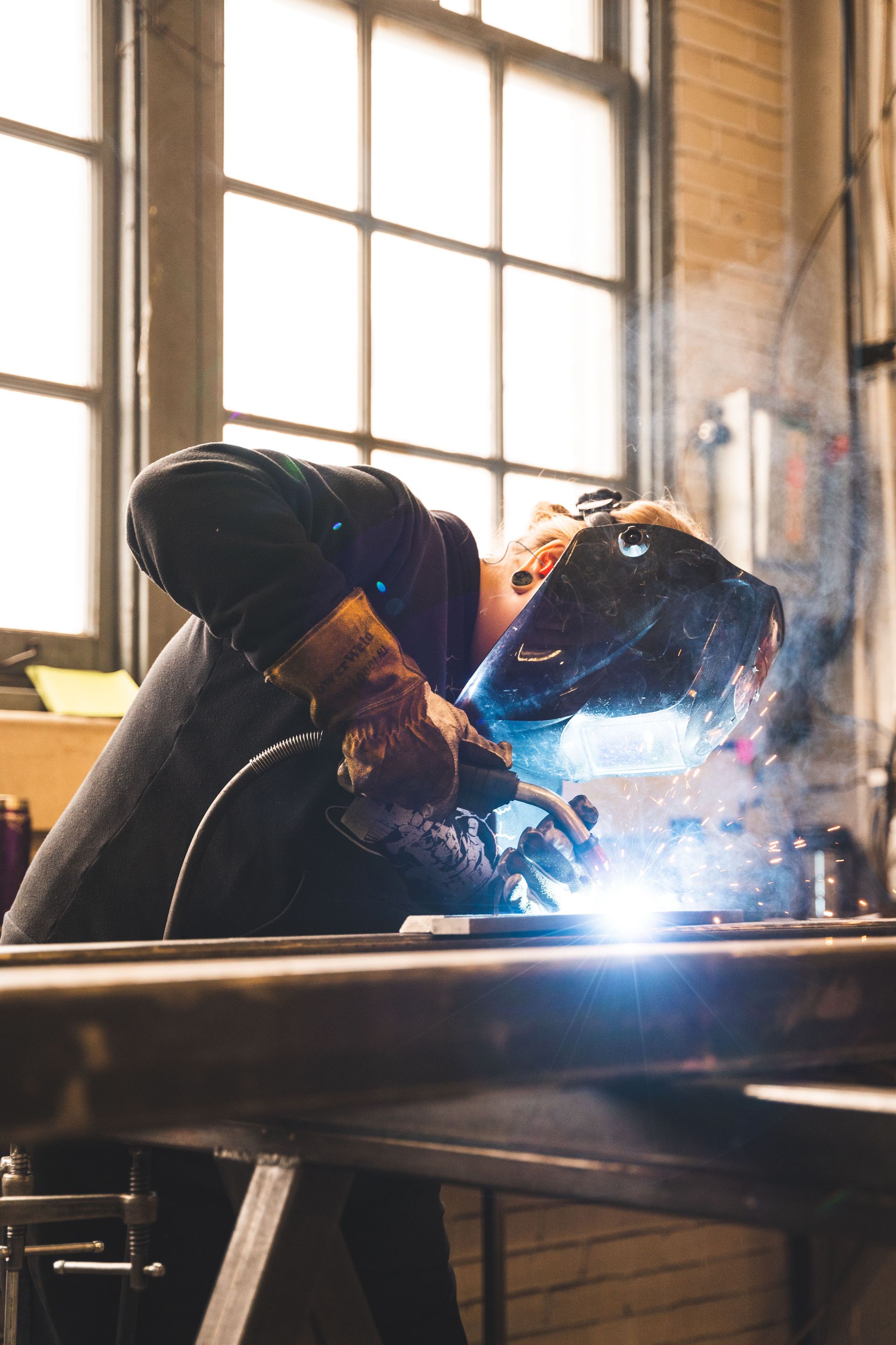 A welder using protective gear in an industrial setting, emitting sparks.